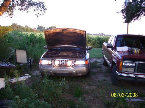 2000 Mercury Grand Marquis - Two vehicles are parked outdoors in a grassy area, with one having its hood up.