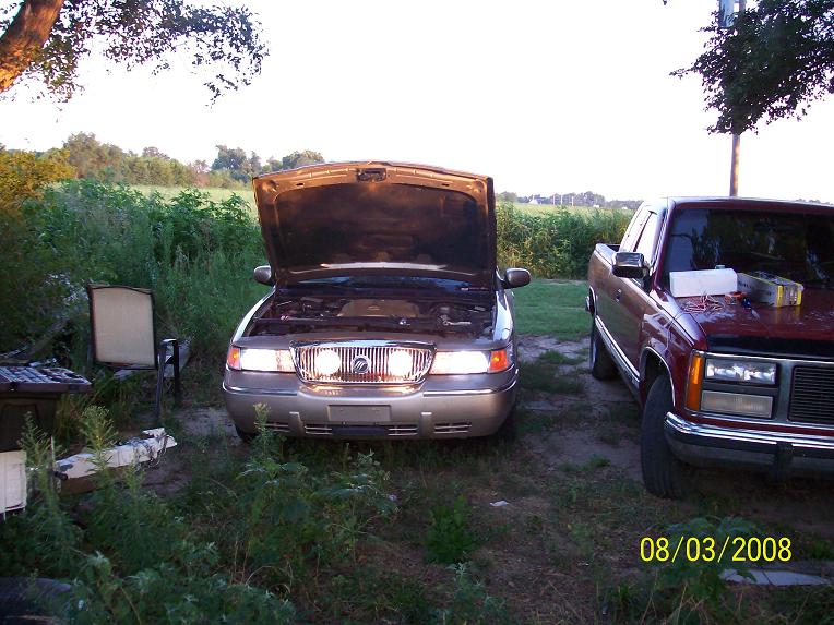 Gold Mercury Grand Marquis with hood open, parked next to a red pickup truck