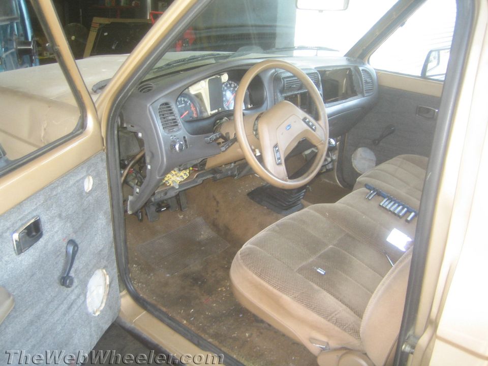 Interior of a tan Ford truck with cloth bench seat and steering wheel, partly stripped