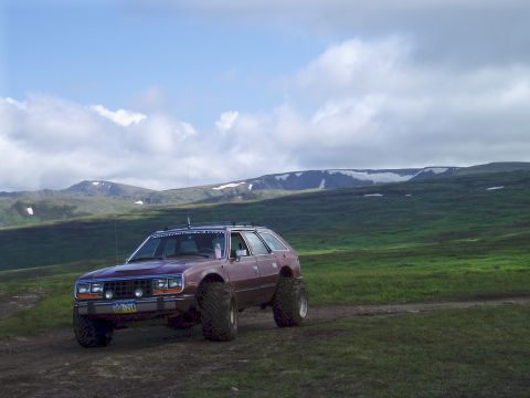 2000 Ford E350 - This lifted station wagon is parked on a dirt road with mountains in the distance under a cloudy sky.