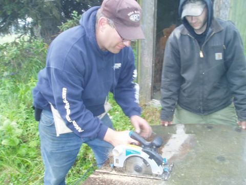 2000 Ford E350 - Two men are working outdoors with a circular saw, cutting a piece of wood.