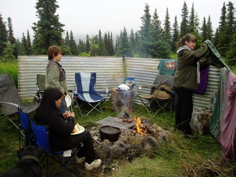 2000 Ford E350 - A group of people enjoy a campfire scene with a corrugated metal backdrop and surrounding trees.