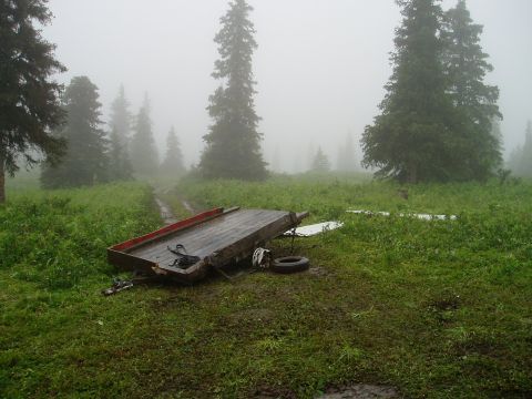 2000 Ford E350 - A trailer has tipped over in a muddy, grassy area surrounded by trees on a foggy day.