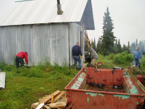2000 Ford E350 - Workers are seen near a cabin, with a trailer and debris in the foreground.