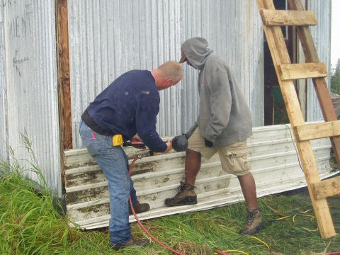 2000 Ford E350 - Two men are working on the side of a building, using tools on corrugated metal panels.