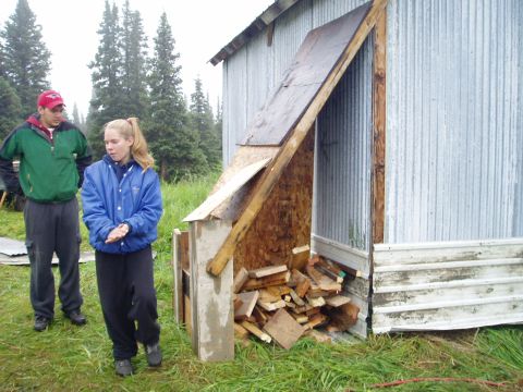 2000 Ford E350 - A man and a woman stand outside a rustic shed filled with firewood, with trees in the background.