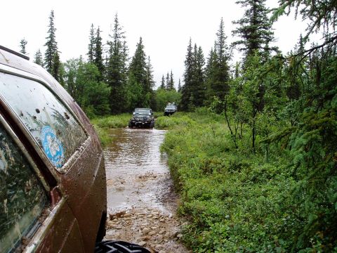 2000 Ford E350 - Multiple off-road vehicles navigate a wet, muddy path through a dense forest.