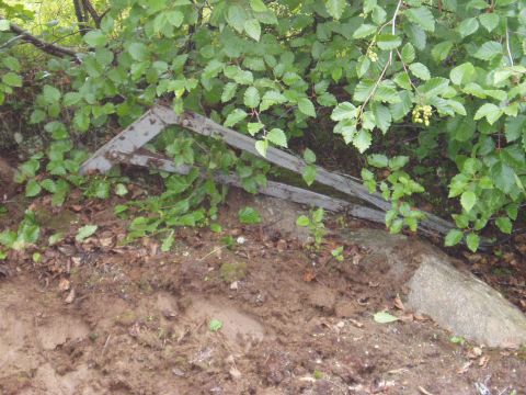 2000 Ford E350 - A metal structure, possibly part of a gate or fence, is partially covered by green foliage and lies on the ground next to a large rock and…