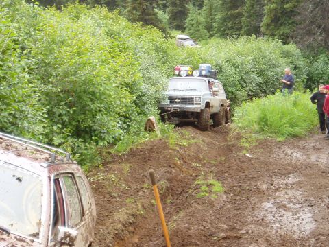 2000 Ford E350 - A light blue Chevrolet K5 Blazer is navigating a muddy trail, with a person standing on the side observing. Another vehicle is partially vi…
