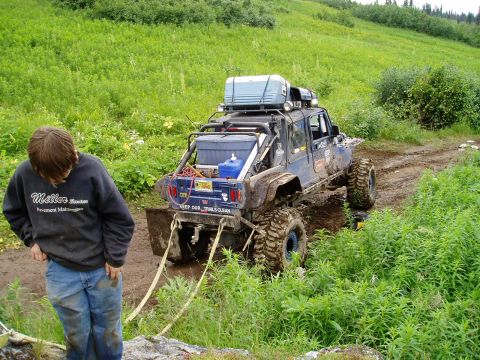 2000 Ford E350 - A blue off-road modified SUV is stuck in mud on a dirt trail, with a person in a dark sweatshirt and jeans standing nearby. The SUV has lar…