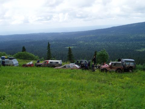 2000 Ford E350 - Several off-road vehicles are parked on a grassy hillside overlooking a vast, forested valley under a cloudy sky. The vehicles include a va…