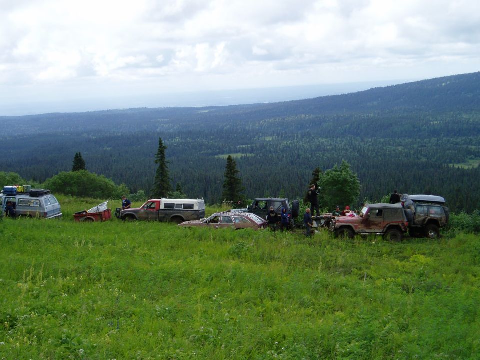 Off-road vehicles parked on a grassy hillside with a forested valley in the background.