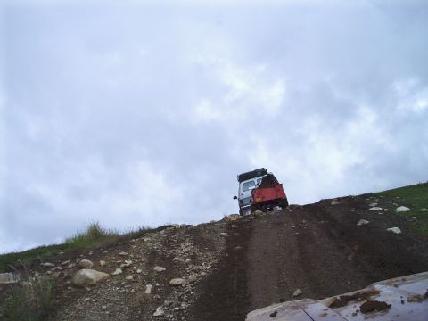 2000 Ford E350 - A white van with a red trailer is parked on a dirt hill under a cloudy sky.