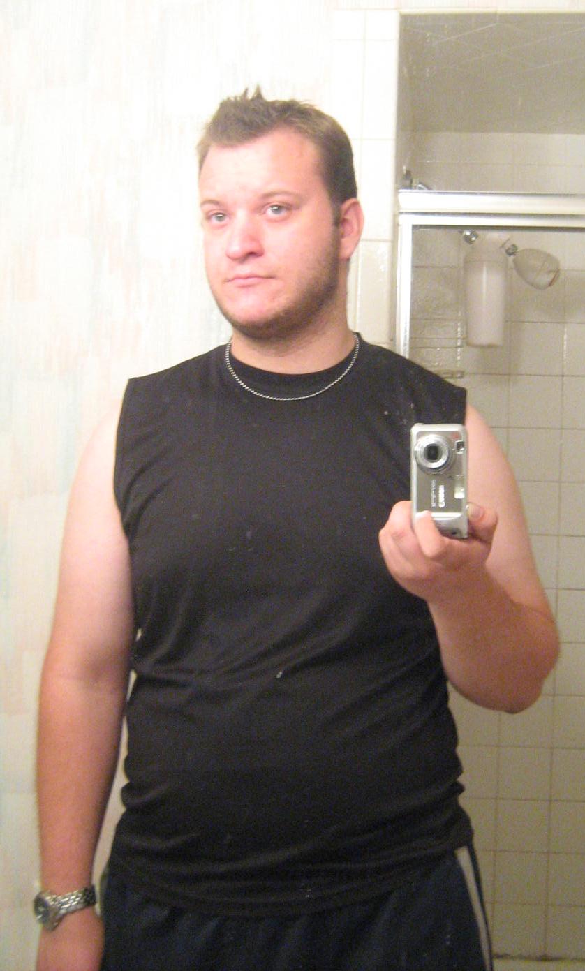 Man in a black sleeveless shirt taking a bathroom mirror selfie