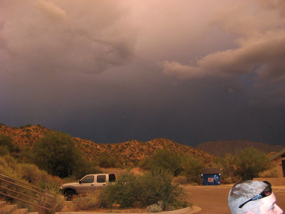 Silver pickup truck parked in desert landscape with stormy sky and blue dumpster.