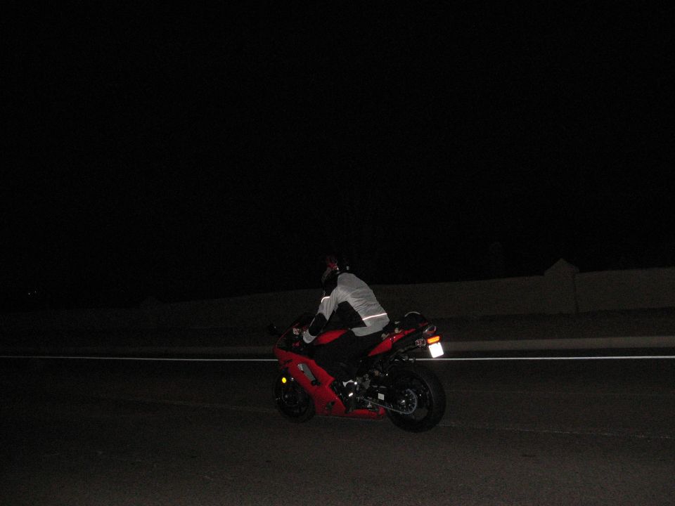 Red sport motorcycle with rider in reflective gear at night.