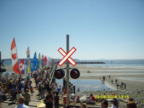 1989 Ford Bronco - A crowd of people are gathered on a pier lined with flags, with a beach and ocean in the background. A railroad crossing signal is visible…