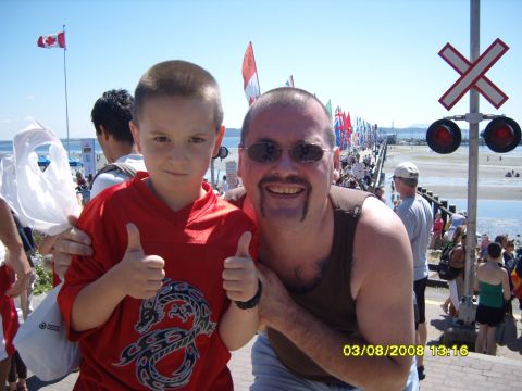 1989 Ford Bronco - A man and a boy pose for a photo in front of a pier with many flags and a railroad crossing signal.