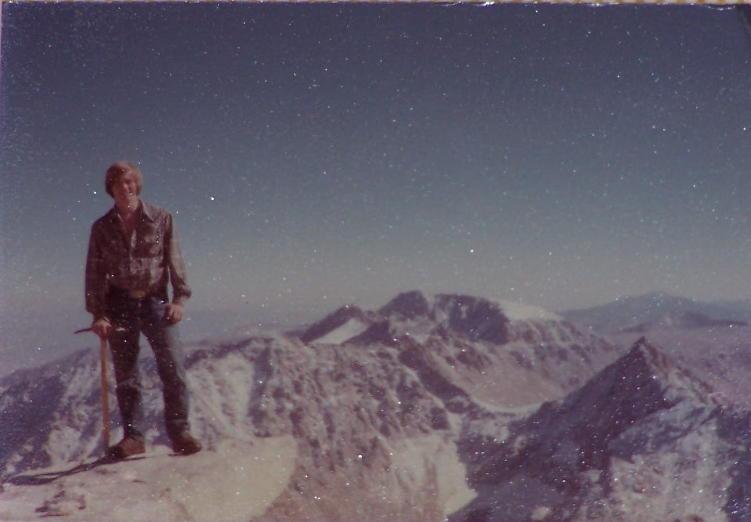 Man on a mountain peak with an ice axe, rocky mountains and starry sky in background