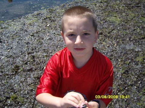 1989 Ford Bronco - A young boy in a red shirt is looking at the camera while standing on a rocky shore next to water. A timestamp in the corner reads "03/08/2…