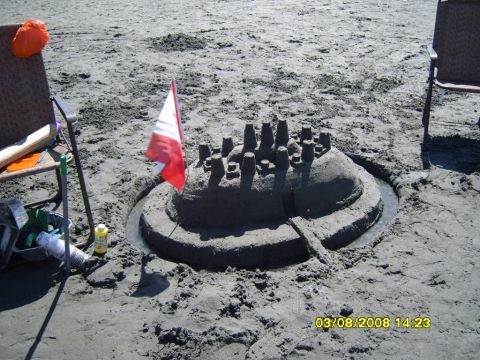1989 Ford Bronco - A sandcastle with a Canadian flag is built on a sandy beach. The sandcastle has a moat filled with water and several turrets on top.