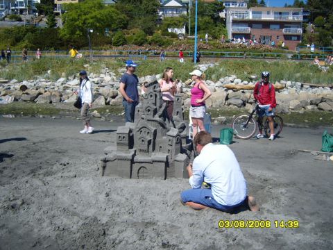 1989 Ford Bronco - A group of people are gathered on a sandy beach, with a large sandcastle in the foreground. In the background, there are buildings, trees,…