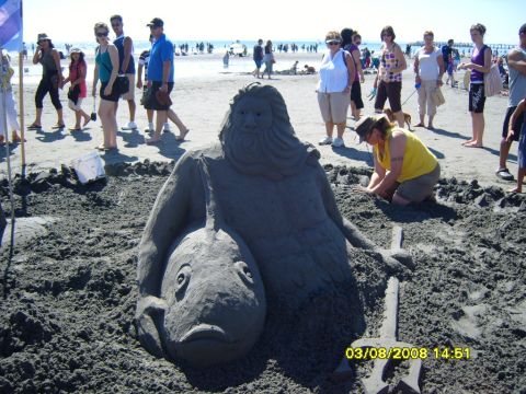 1989 Ford Bronco - A sand sculpture of a mythical creature holding a fish is displayed on a beach with people in the background.