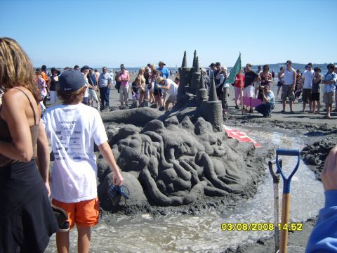 1989 Ford Bronco - A large, intricate sandcastle is the main focus of the image, with a crowd of people gathered around it on a sunny beach. A shovel is visib…
