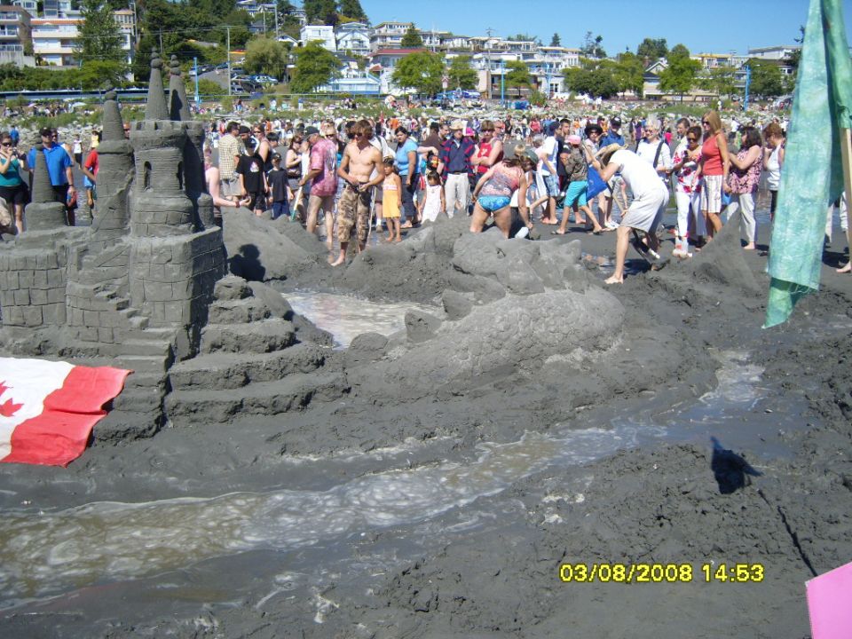 Sandcastle on a beach with people and a Canadian flag.