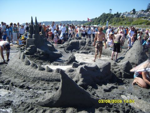 1989 Ford Bronco - A large sandcastle resembling a dragon or castle is the main focus of this beach scene. Many people are gathered around watching or partici…