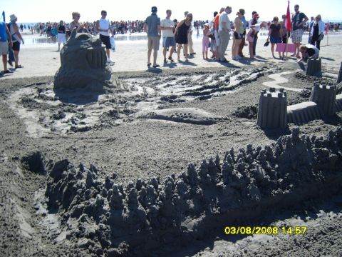 1989 Ford Bronco - A large, intricate sandcastle is built on a beach, with many people in the background. The sandcastle features towers, walls, and a large c…