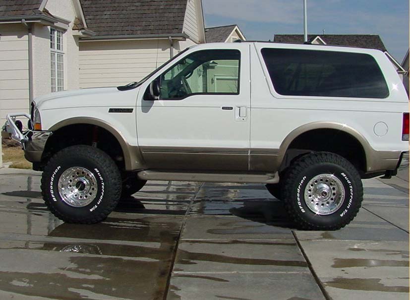 Lifted white two-door SUV with tan lower trim and BFGoodrich Mud-Terrain tires, side view on wet driveway