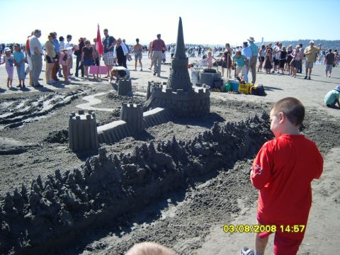1989 Ford Bronco - A large sandcastle is the main focus of this beach scene, with a young boy in a red shirt standing in the foreground. Numerous people are v…
