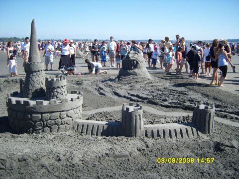 1989 Ford Bronco - A large sandcastle is displayed on a beach with many people in the background. The sandcastle is designed to look like a medieval fortress…