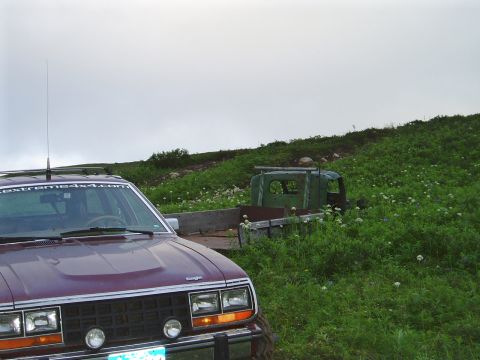 2000 Ford E350 - A maroon AMC Eagle sedan is parked in front of a grassy hill with an old green truck cab in the background.