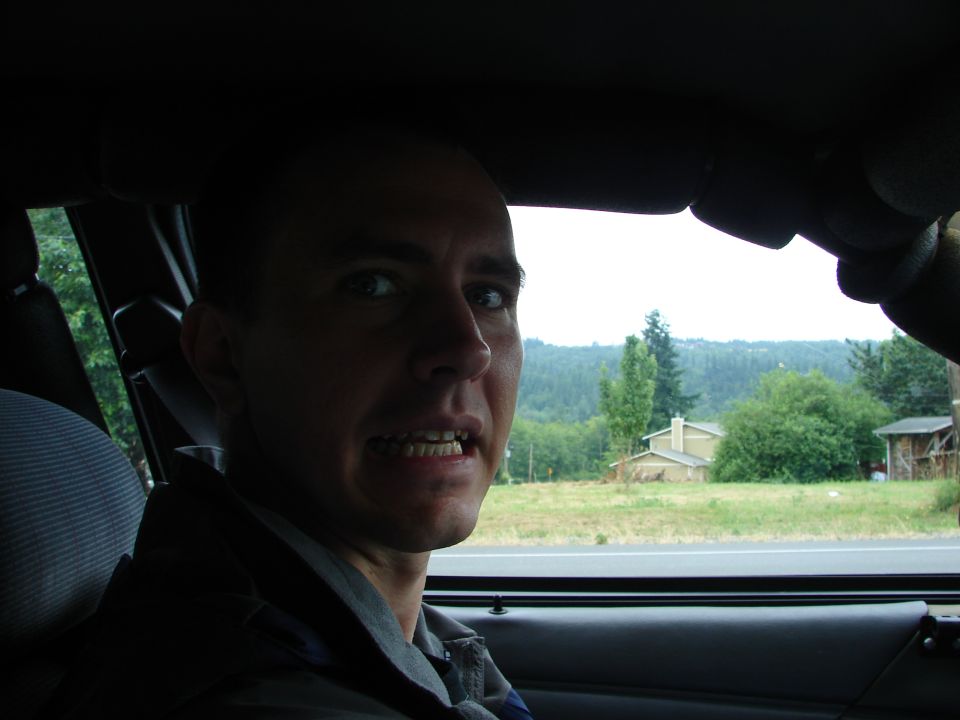 Man looking out the passenger window of a car with a rural landscape outside.