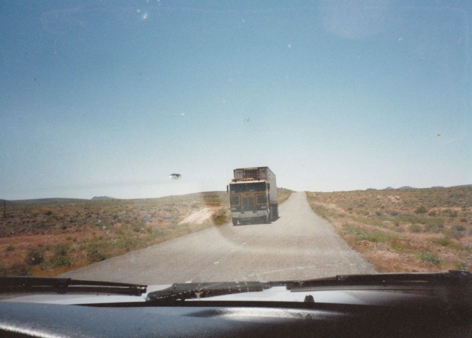 Semi-truck driving on a road in a desert landscape.