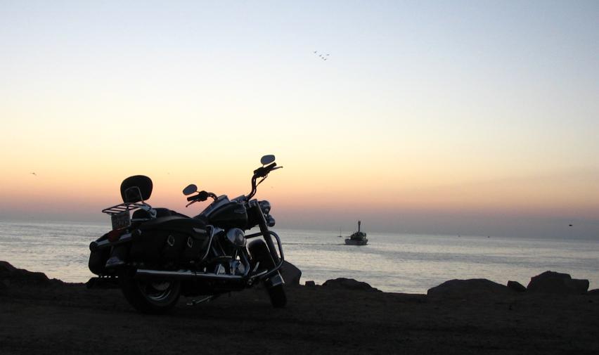 Black touring motorcycle silhouetted on coastal rocks at sunset over the sea