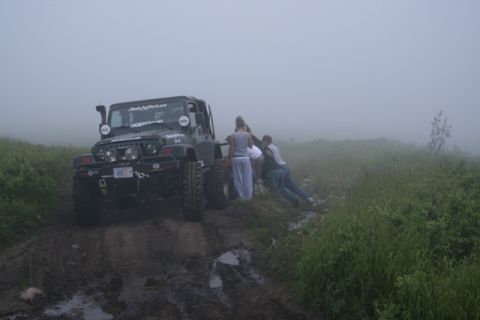1990 Chevrolet Suburban - People push a Jeep Wrangler through a muddy, off-road path on a foggy day.
