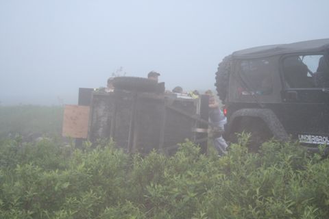 1990 Chevrolet Suburban - An off-road vehicle is parked beside a trailer that has tipped over in a misty, brush-filled area.