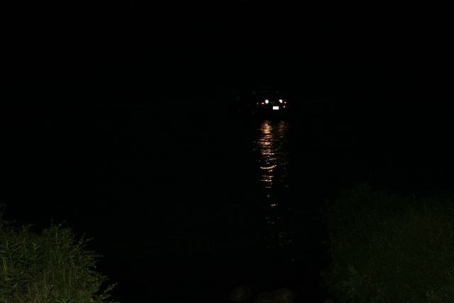 Vehicle with illuminated taillights and headlights reflected in water at night