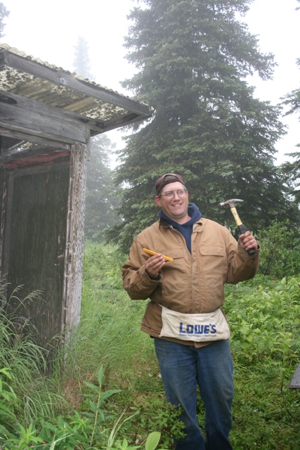 1990 Chevrolet Suburban - Man with hammer and corn cob stands by an old wooden structure in a foggy, wooded area.