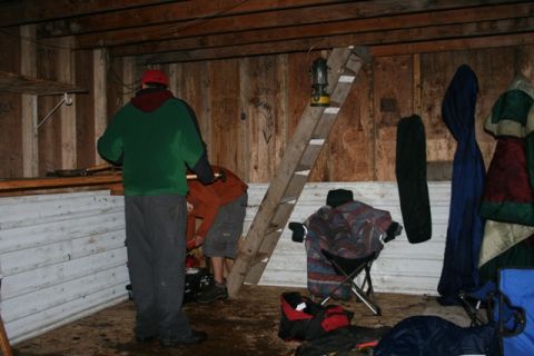 1990 Chevrolet Suburban - A cluttered interior scene within a wooden structure, people and camping equipment.