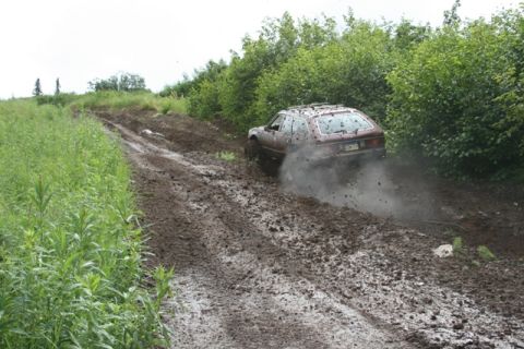 1990 Chevrolet Suburban - A brown station wagon drives off-road through thick mud, kicking up a cloud of dust and debris. The vehicle navigates a steep, rutted dirt…