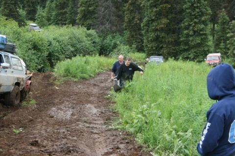 1990 Chevrolet Suburban - A light blue Chevrolet Suburban is stuck in thick mud on a trail, with two men attempting to free it. Other off-road vehicles are visible f…