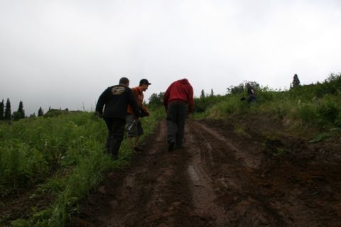 1990 Chevrolet Suburban - Four people walk up a muddy, rutted dirt path on a grassy hillside under an overcast sky. Two of the people are walking away from the camer…