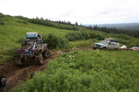 1990 Chevrolet Suburban - Two off-road vehicles navigate a muddy trail through a grassy, wooded hillside under an overcast sky. The vehicle in the foreground is a he…