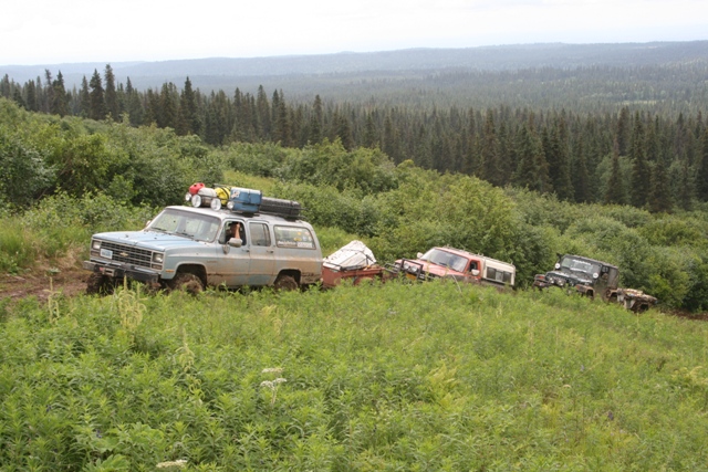 Light blue Chevrolet Suburban off-roading with other vehicles in a forest.