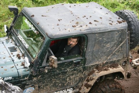 1990 Chevrolet Suburban - A mud-covered green Jeep Wrangler is stuck in the mud with a driver looking out the window. The vehicle has a snorkel and stickers on the w…