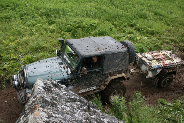 Muddy green Jeep Wrangler with trailer on a trail.